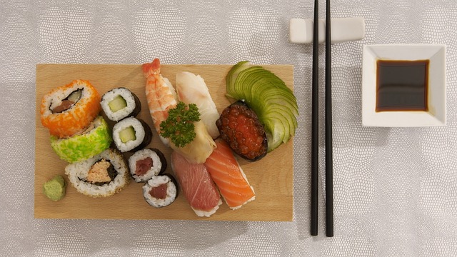 imagem de combinado de comida japonesa em uma tábua, com hashi ao lado e pote branco com molho shoyo